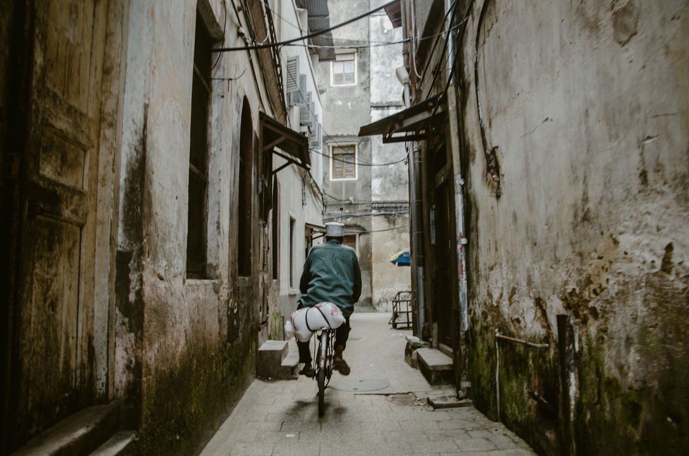 A cyclist riding through a narrow Stone Town alleyway